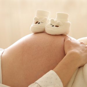 Pregnant woman cradling her stomach with two small shoes resting on top