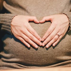 Pregnant woman holding her stomach and making a heart-shape with her hands