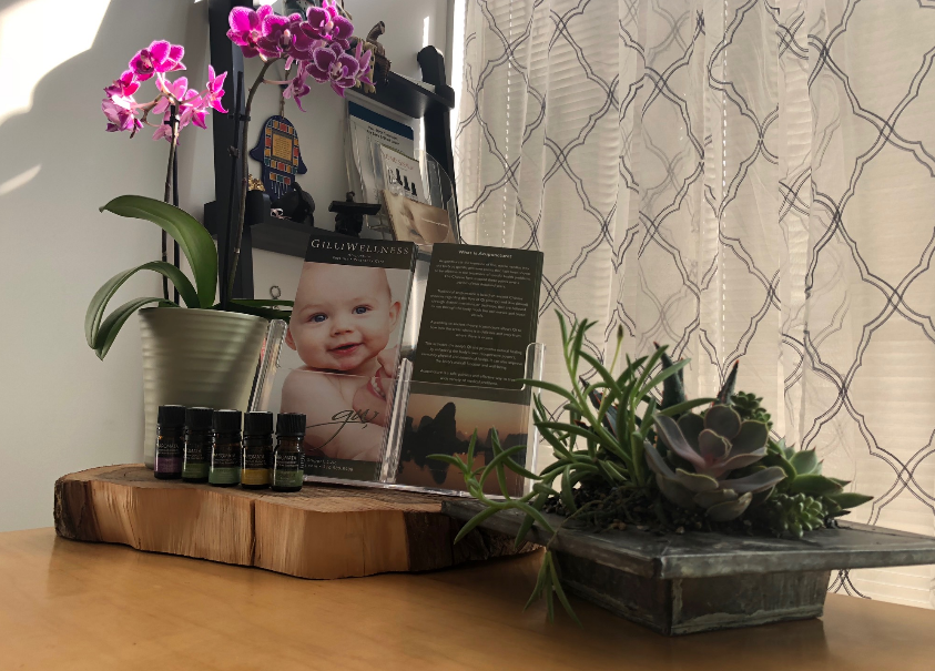Front desk of the office with small aromatherapy bottles, pink flowers, a plant, brochure, and a white curtain in the background, creating a soothing and welcoming atmosphere