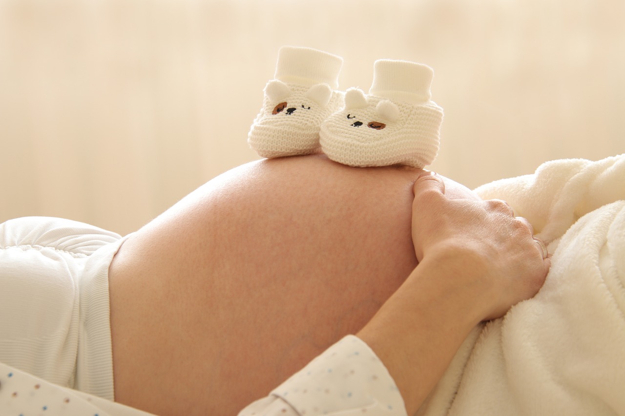 Pregnant woman cradling her stomach with two small shoes resting on top