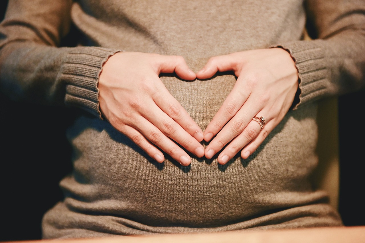 Pregnant woman holding her stomach and making a heart-shape with her hands