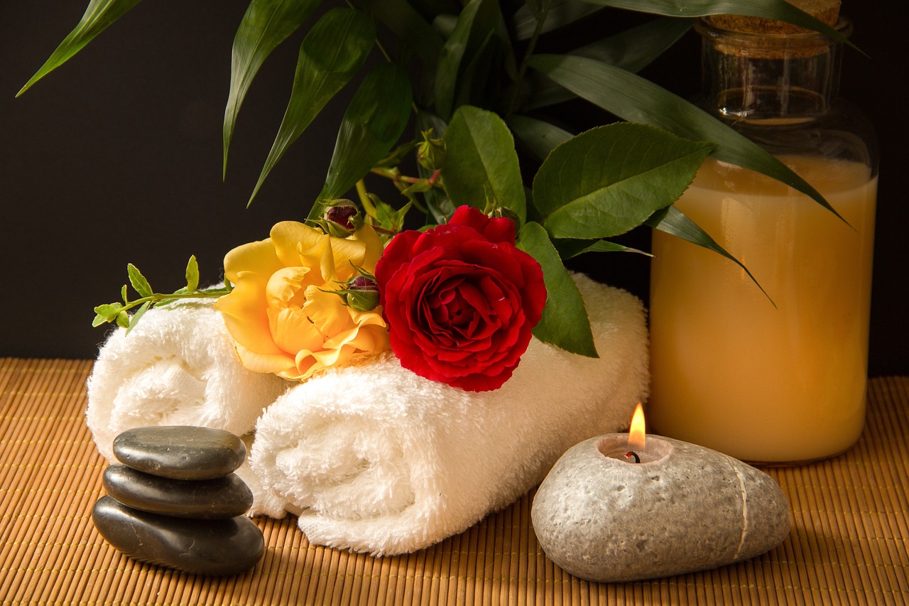 Wellness and treatment representation: Two white towels, stacked rocks, a candle nestled inside a smooth rock, and two flowers delicately placed on top of the towels, creating a serene and relaxing scene